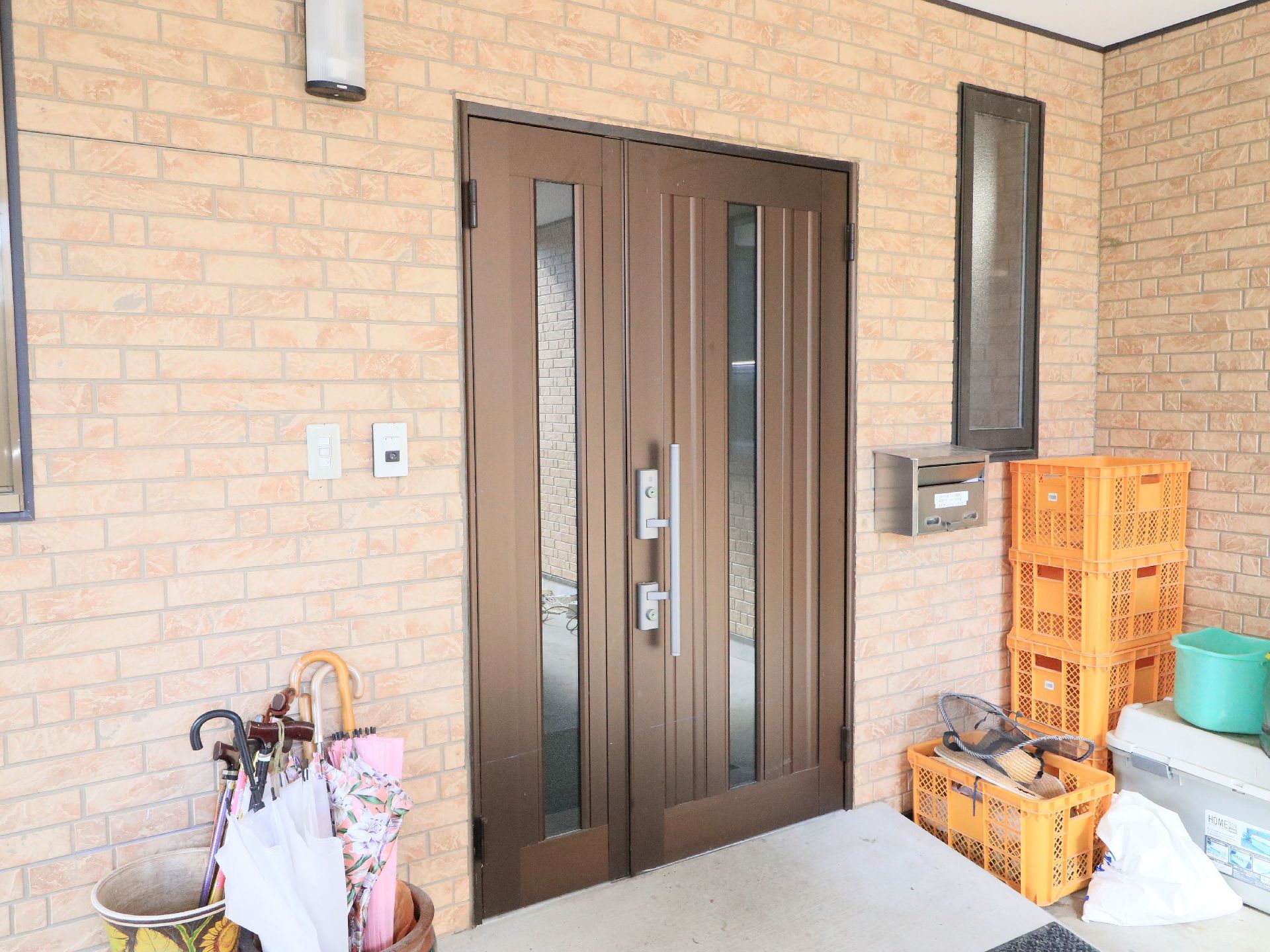 施設玄関は明るい色のレンガ調の壁に外灯やポスト、一般住宅と同様の片開き式のサッシ扉が完備されている。
