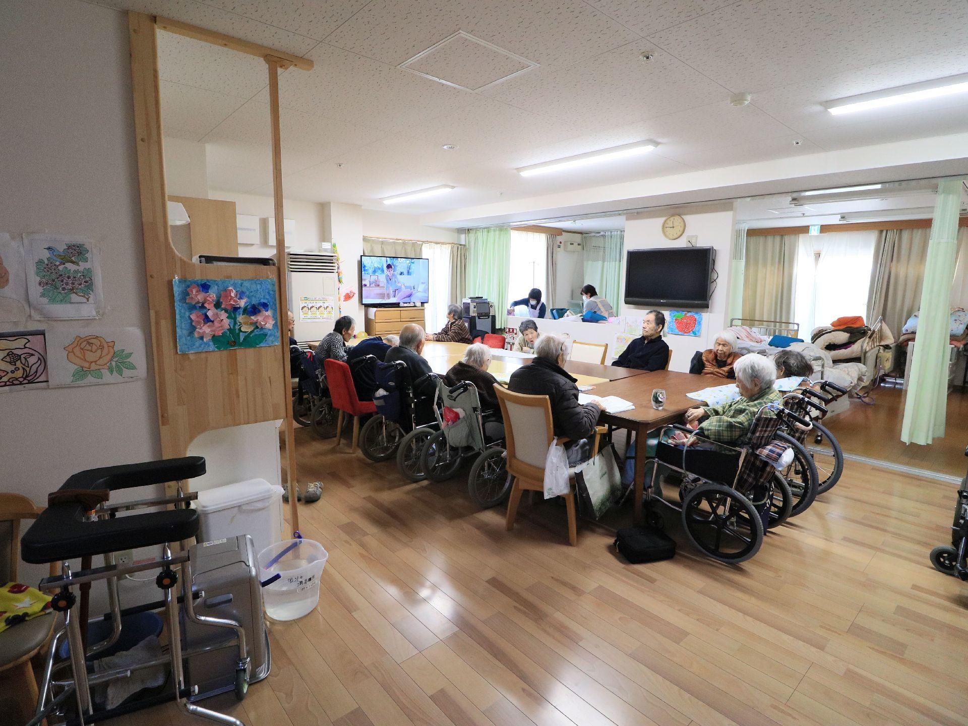 テレビの点いている共有スペースでは、テーブルが寄せあわせて設置されており、入居者様たちが着席している。