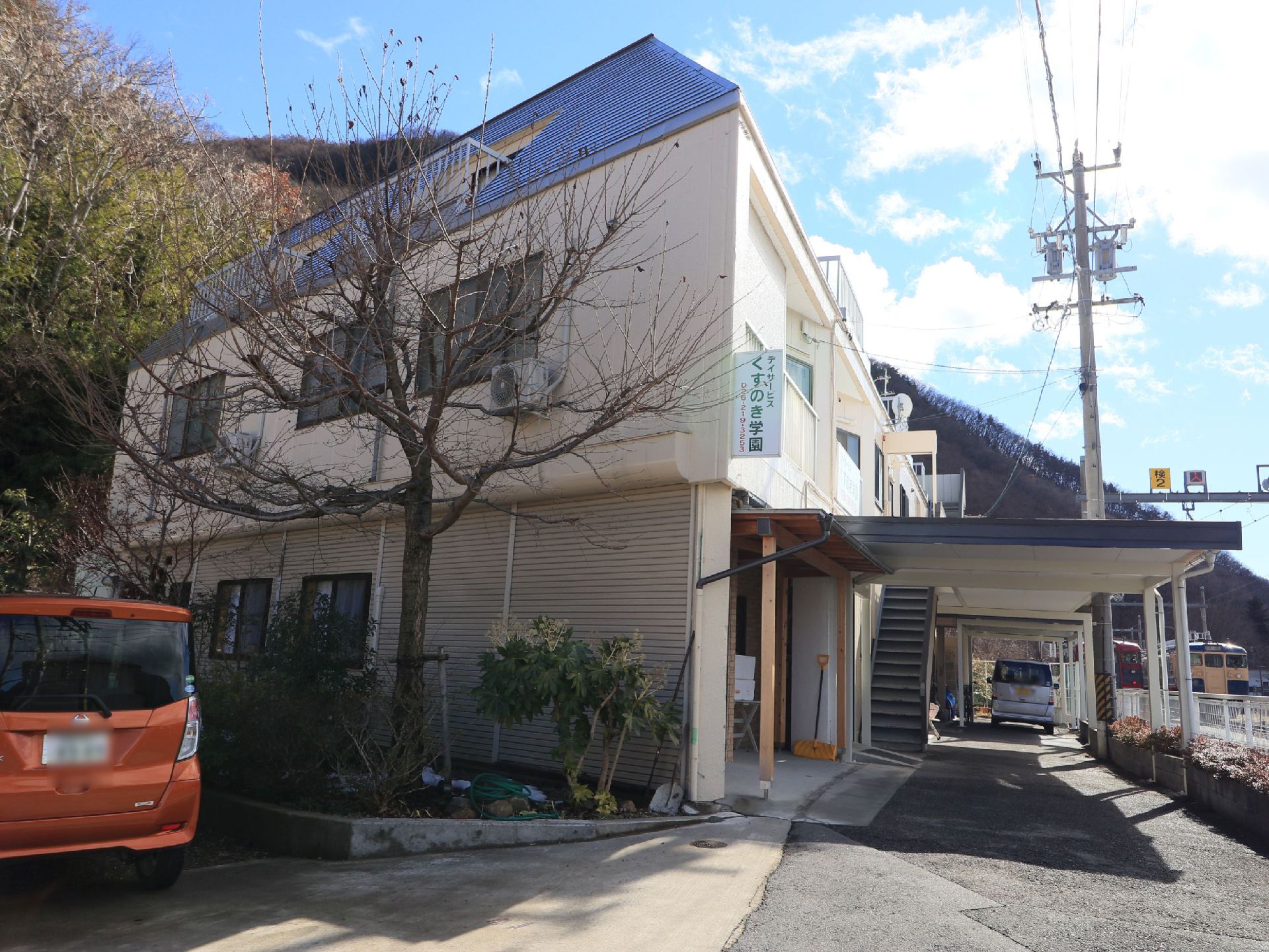 小高い山の麓に立地する1階建て施設の様子である。脇道に雪が残っている。自然豊かな環境での豊かなシニアライフを提供する。
