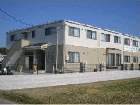 白とベージュ色をした木造地上2階建ての施設である。外階段が設置されている。敷地は黒いフェンスで囲われている。