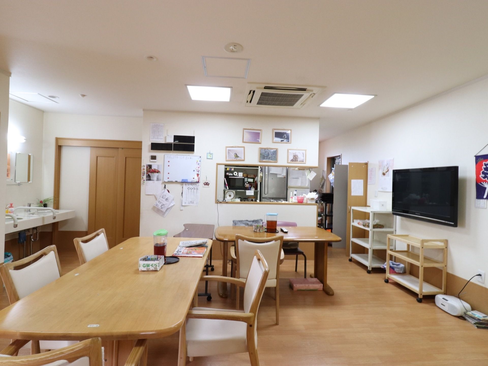 ダイニングルームには大型テレビがあり、床にはラジカセも置かれている。また壁にはホワイトボードがあり、写真が飾られている。