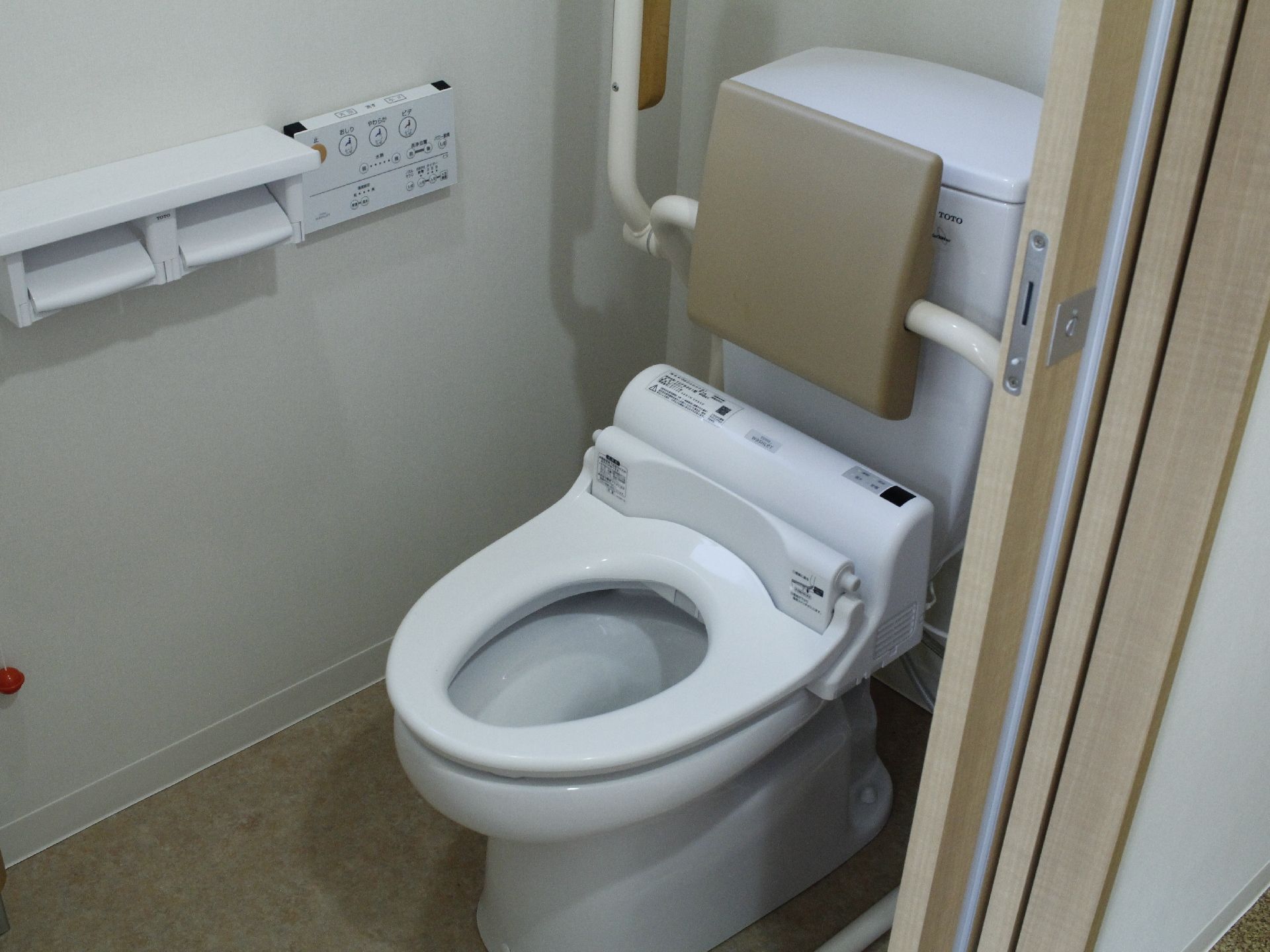 トイレタンクの前には背当てパッドが設置されている。横にはパイプで繋がった手すりがあり、必要な時に下げて使えるようになつている。