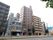 マンションやビルが立ち並んでいる大きな道路に面して建てられている施設周辺の画像。施設は一際目立つ10階建て。