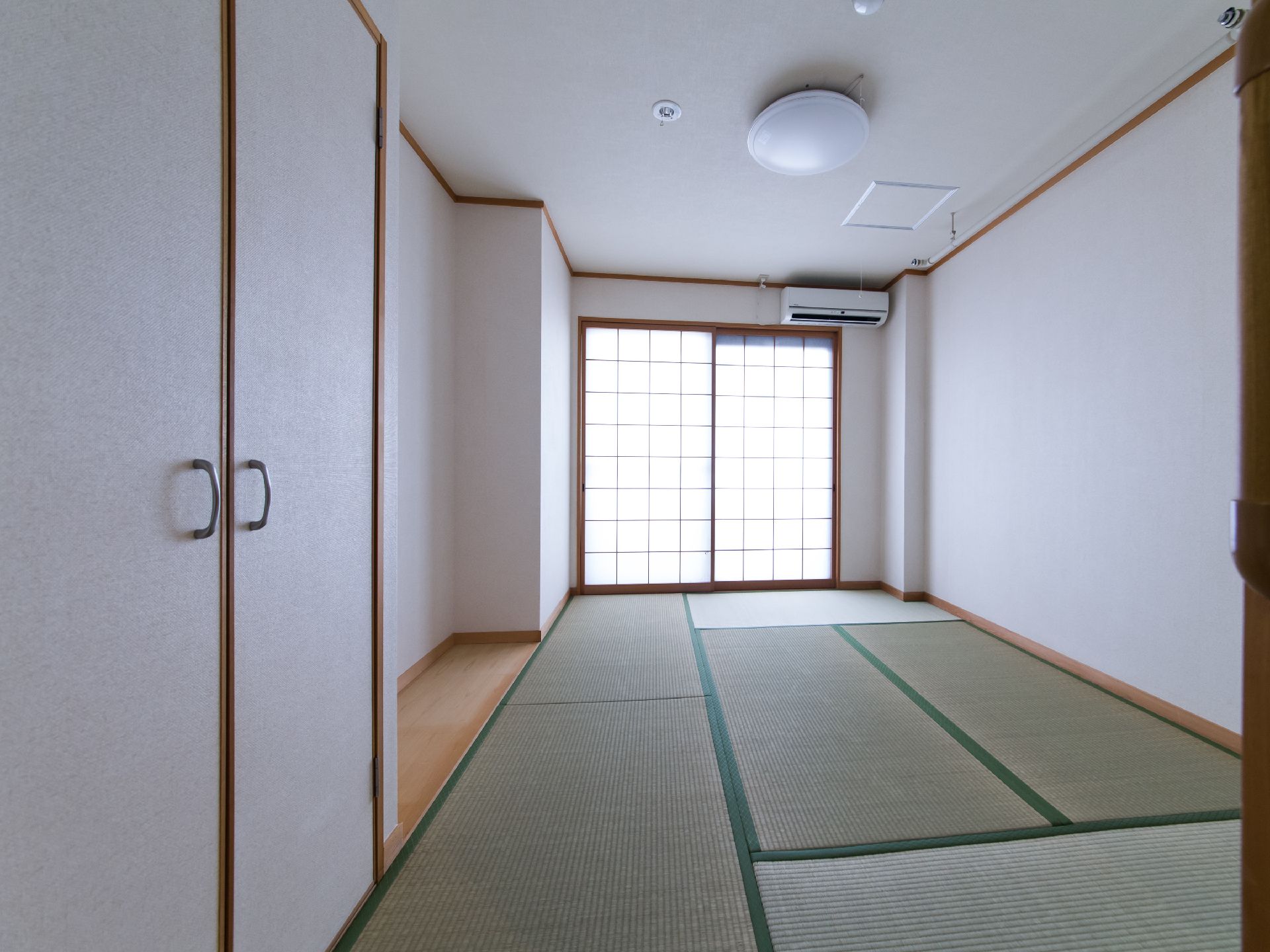 施設には畳敷きの居室がある。掃き出し窓には障子があり、上の壁にはエアコンが1台設置されている。天井に丸い照明がある。