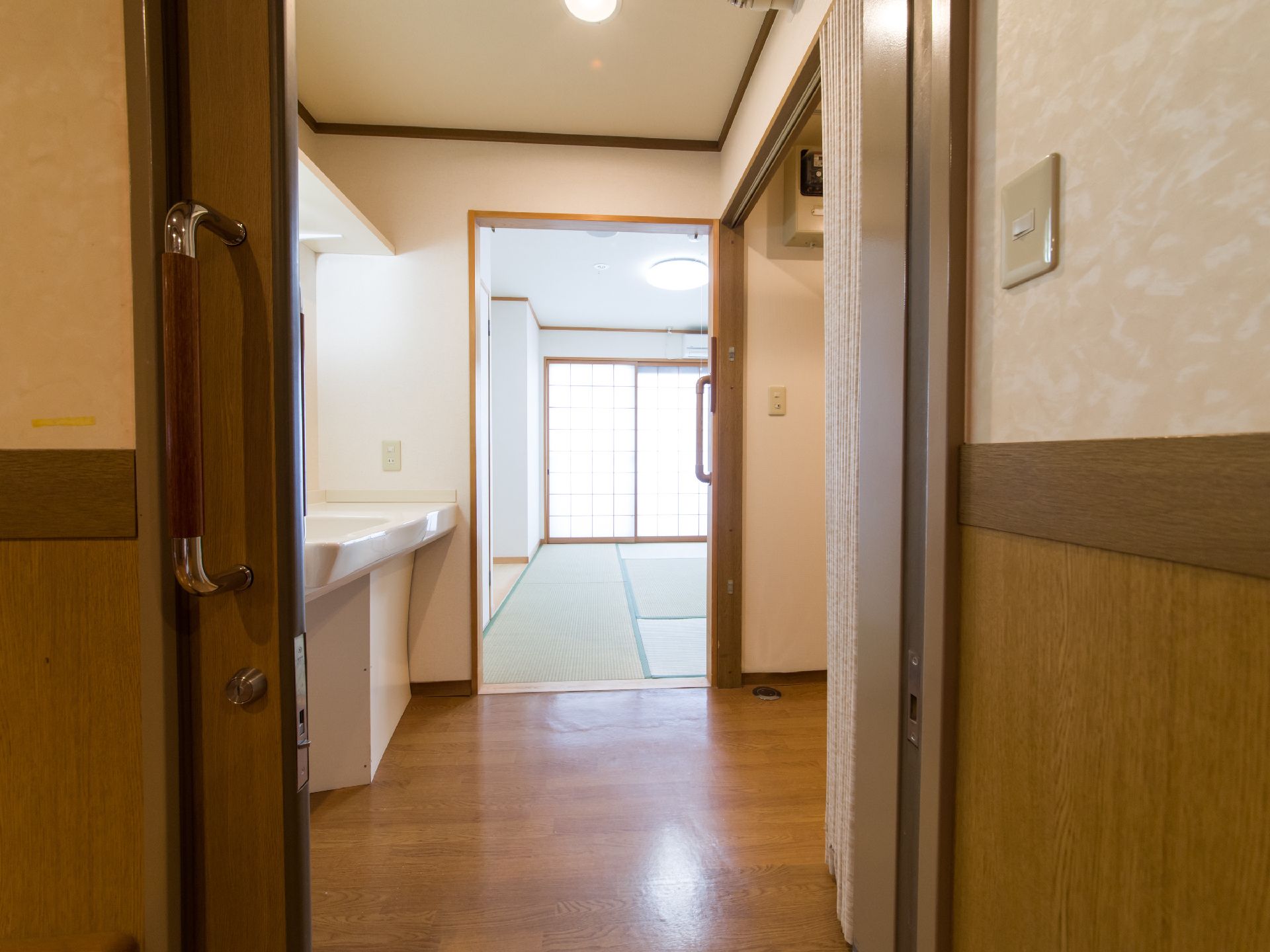 居室の入り口の扉は木製の引き戸で、大きな握りハンドルと鍵が設置されている。和室の手前にはフローリングの空間がある。