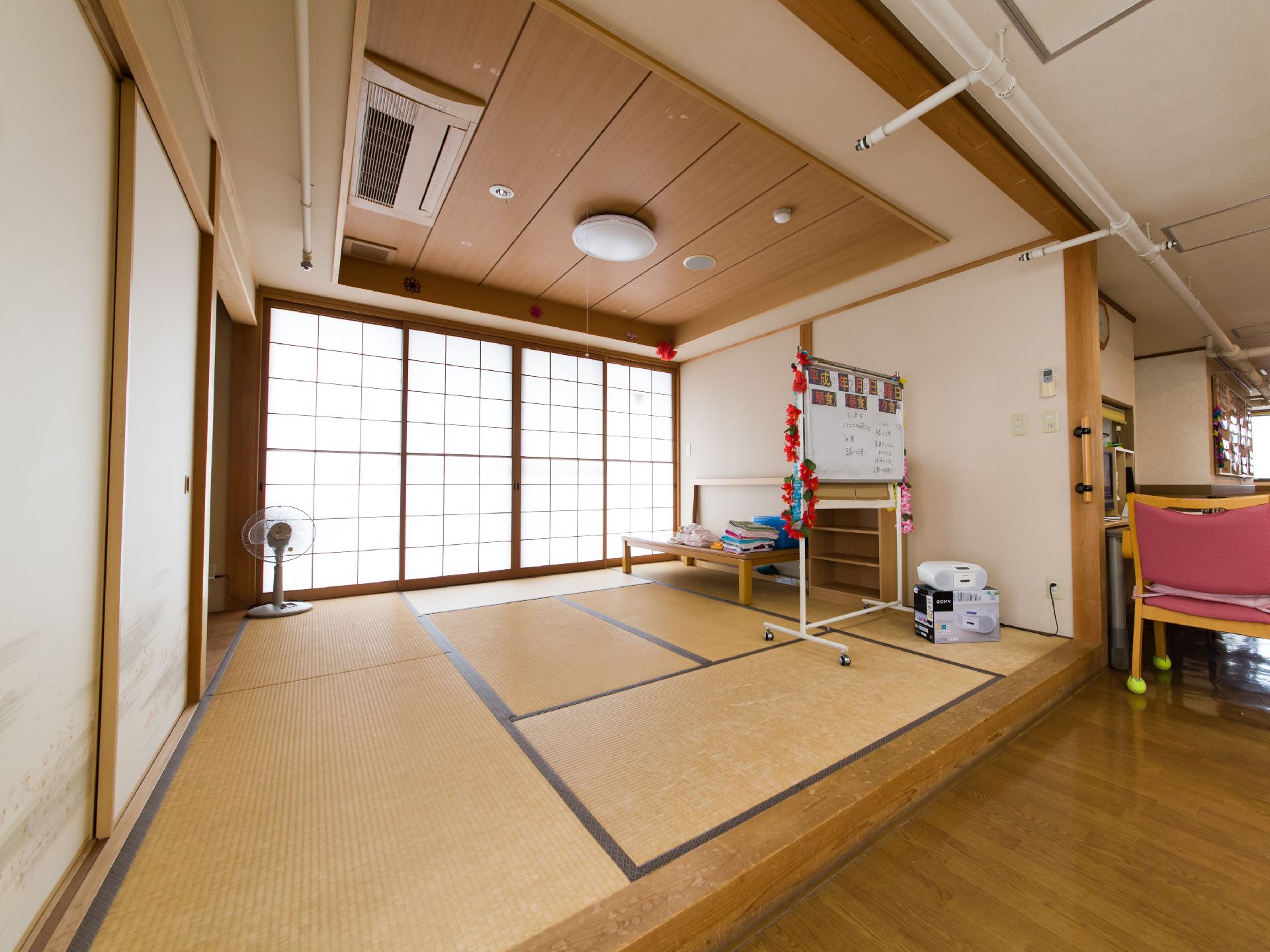 リビングの横には畳敷きの空間が設けられている。1方向には4本の障子があり、日差しが射し込んでいる。扇風機が置かれている。