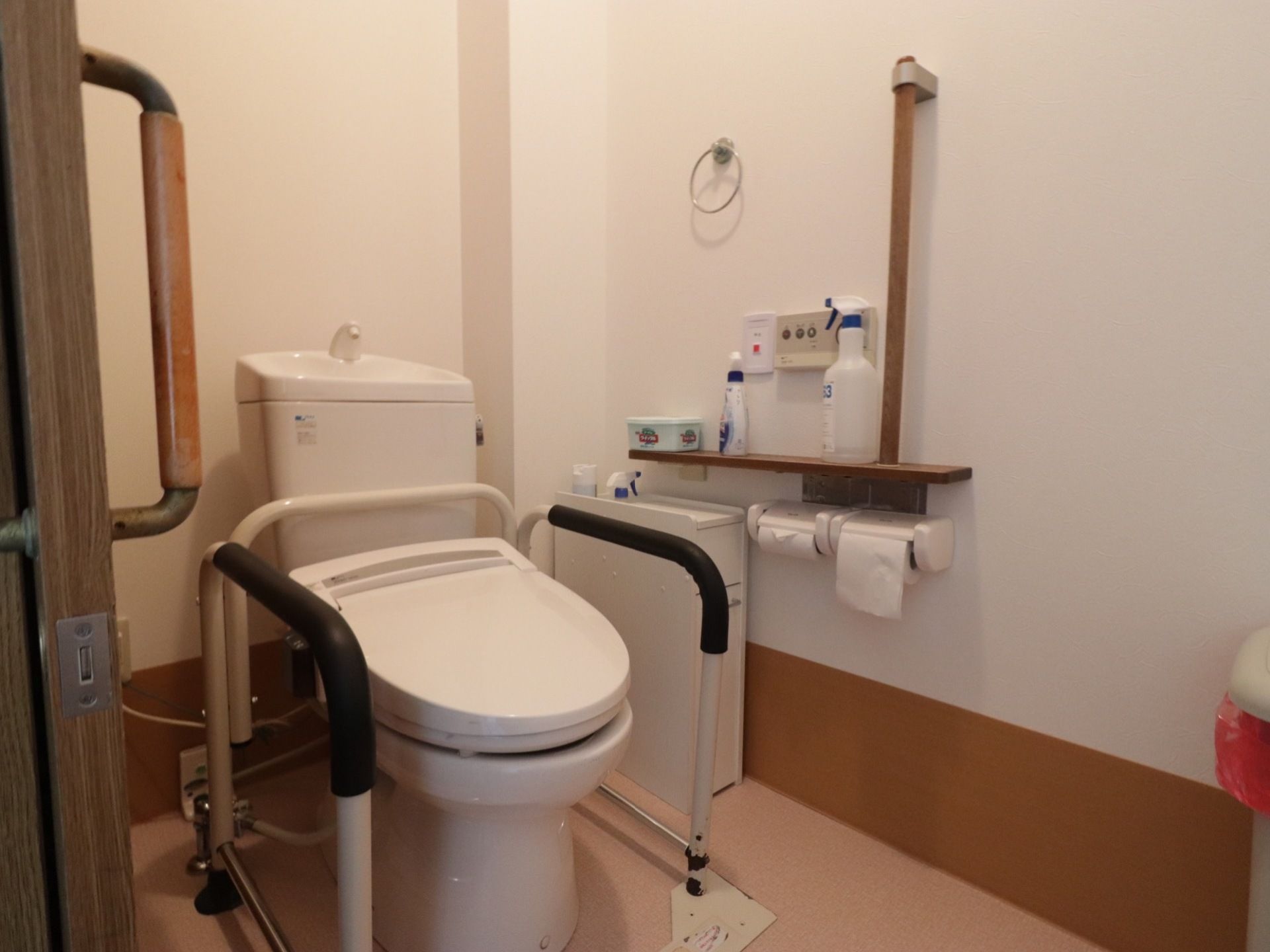 トイレのドアは引き戸タイプで、便座の横には体を支えるときに握る手すりが設置されている。壁には縦長の手すりやタオル掛けがある。