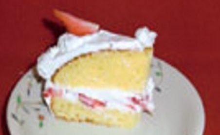 お皿に切り分けられたケーキが載っている。スポンジケーキにたっぷりホイップクリームが塗られ、イチゴで彩られている。