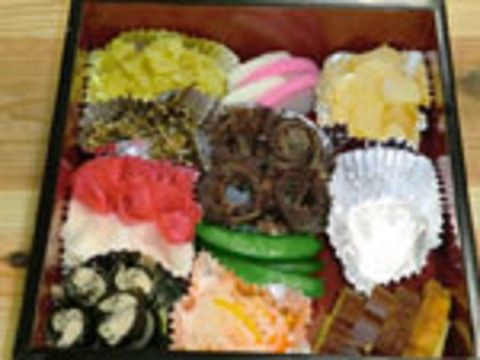 栗きんとんやなます、昆布巻き、かずのこ、かまぼこ、伊達巻などのおせち料理が重箱に彩りよく詰められている。