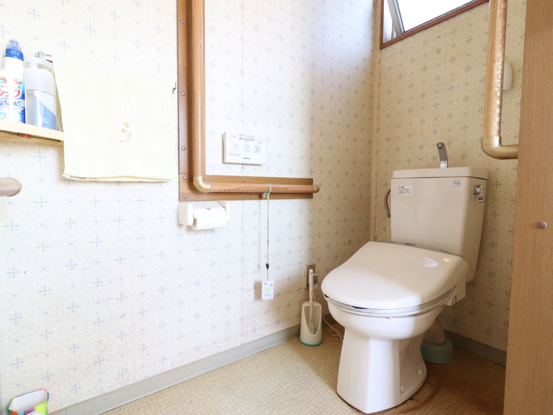 トイレは白色と木を基調にできている。便座の両サイドには手すりが設置されており、手すりからはナースコールがつるされている。