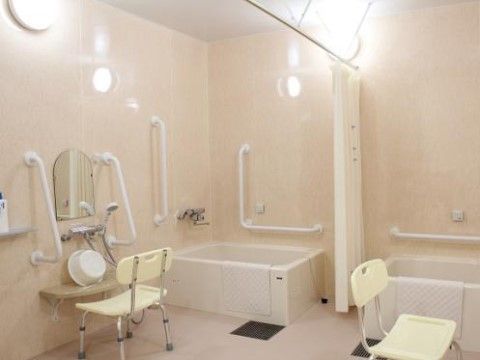 浴槽と洗い場が複数設置されている共用の浴室。天井にカーテン、壁には手すりが取り付けられている。シャワーチェアが準備されている。