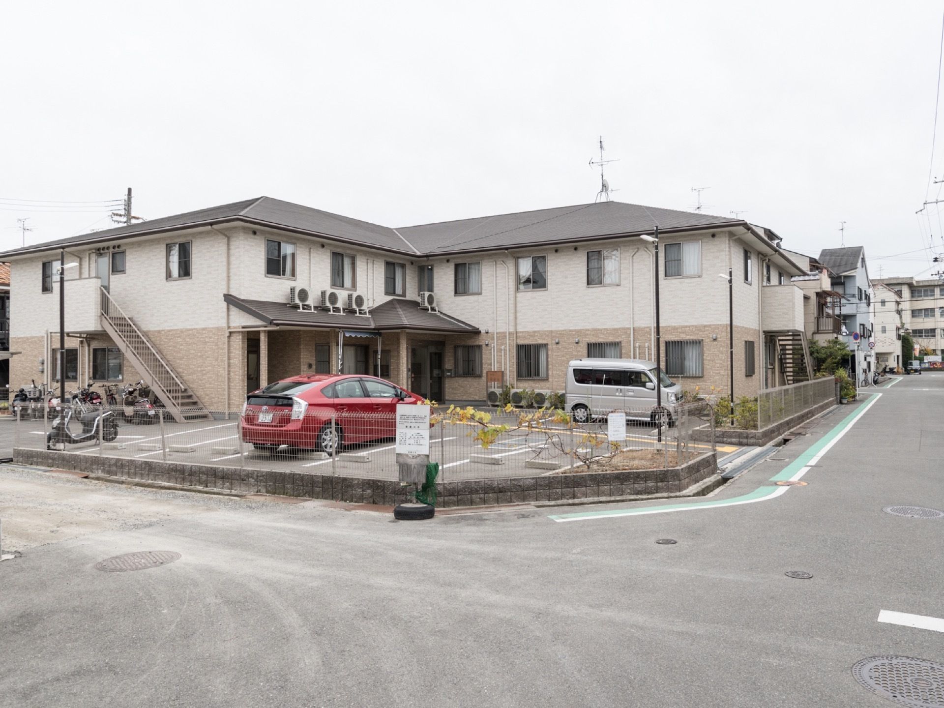 施設を外から見た様子。２階建てのアパートに近い構造になっており、アスファルト舗装された敷地内は駐車場になっている。