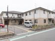 施設の建物は１階部分と２階部分で外壁の色が違うデザインになっている。入り口以外は各エアコンの室外機が地面に設置されている。