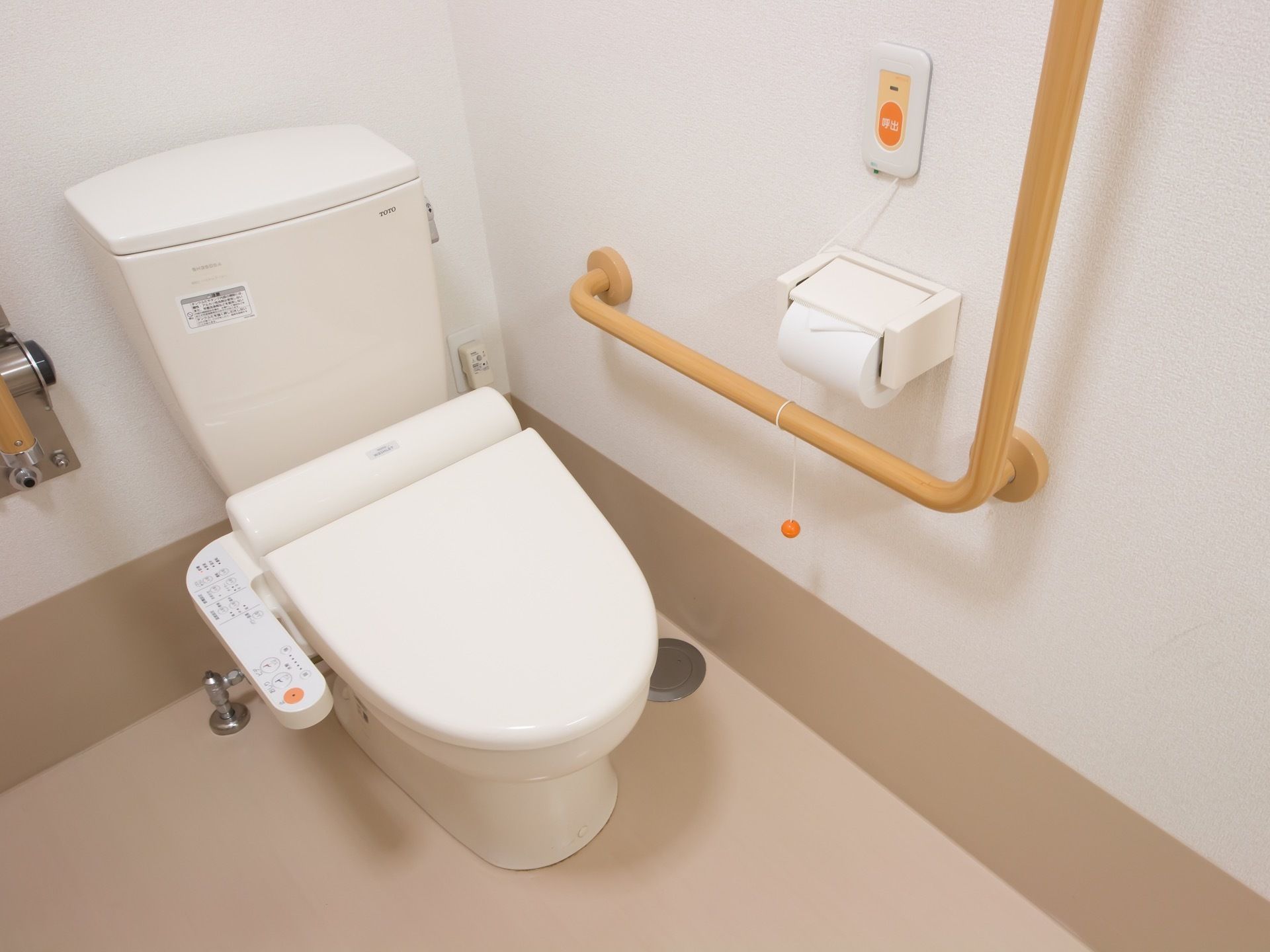 トイレの便座の横には温水洗浄便座の操作ボタンが設置されている。壁には非常ボタンと手すりが備えつけられている。