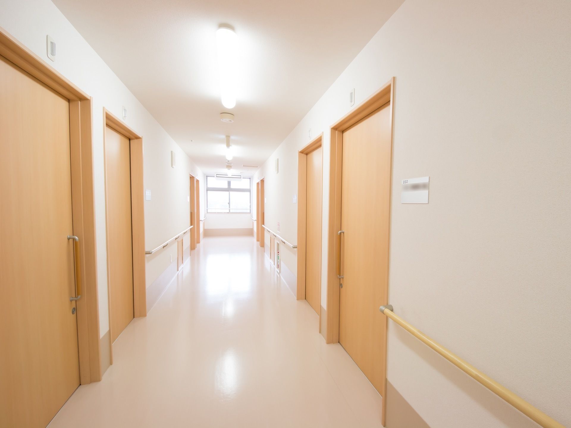 廊下の突き当りには窓がある。両側に居室のドアが並び、手すりが取りつけられている。ドアの横にネームプレートが貼られている。