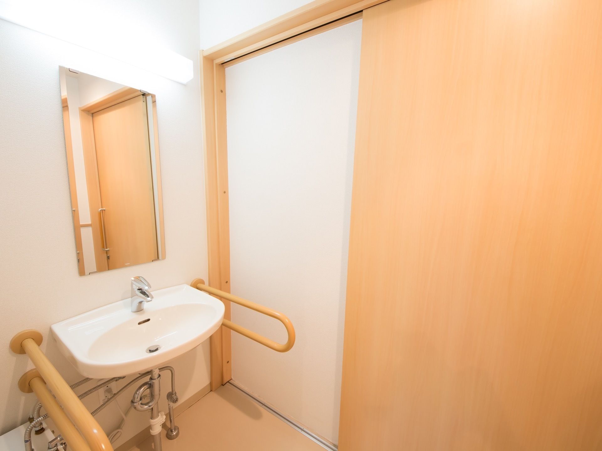 居室内のトイレは引き戸になっている。流し台があり、両側に固定式の手すりが取りつけられている。壁に鏡がある。