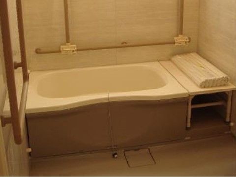 ベージュを基調とした浴室である。浴槽のそばには段差を作らないための台が置かれている。全面に手すりが設置してある。