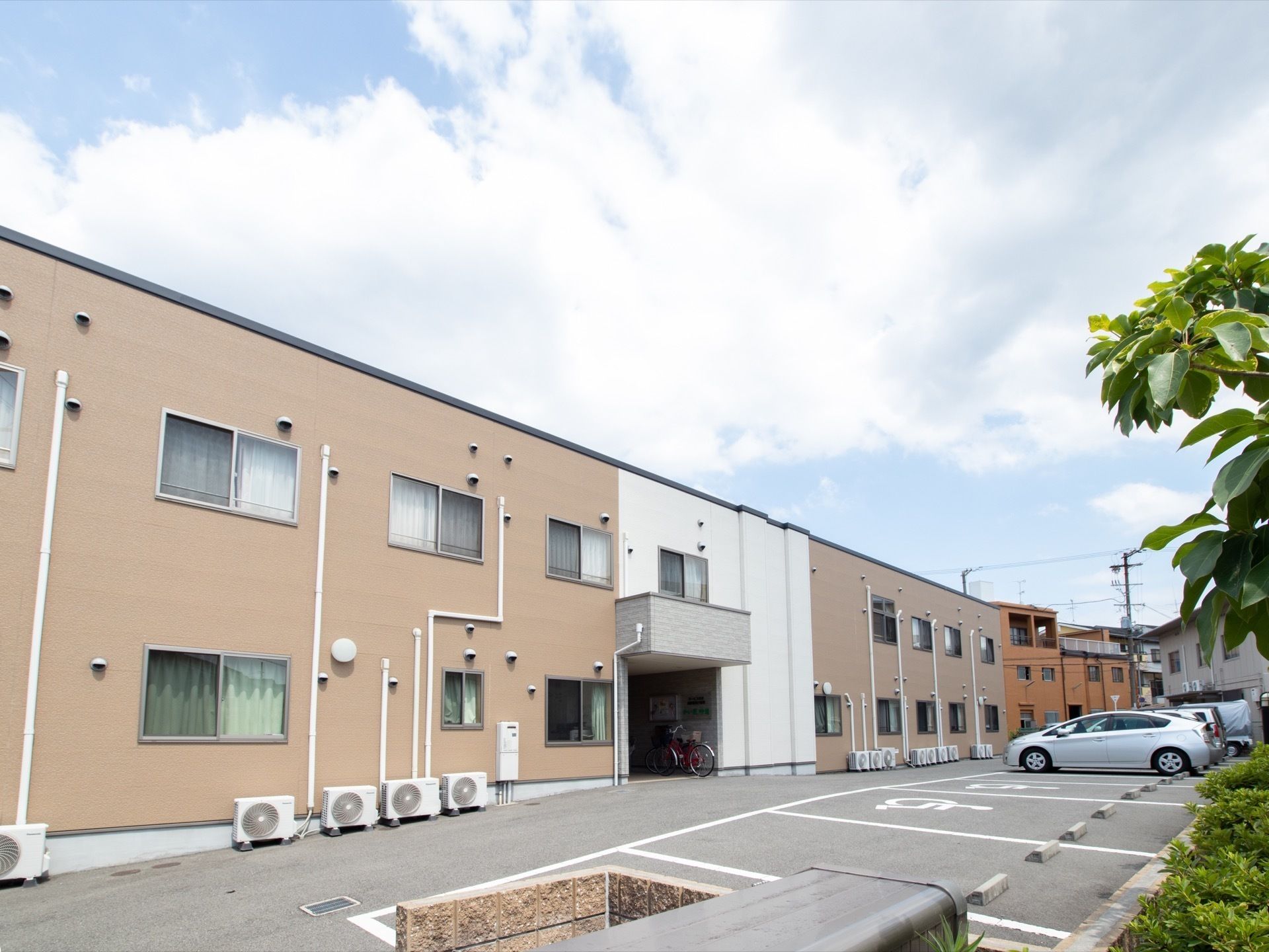 ベージュと白の外壁の施設建物の裏に設けられた駐車スペース