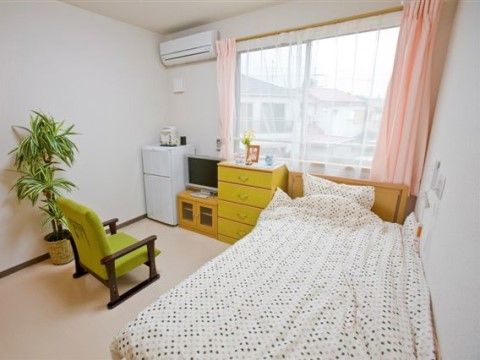 ベッドや家具、冷蔵庫、1人掛けのソファが置かれた居室のイメージ