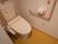 便器の両側に手すりが設置されたトイレである。左側に緊急時呼び出しボタンが備えてあり、長い紐もついている。