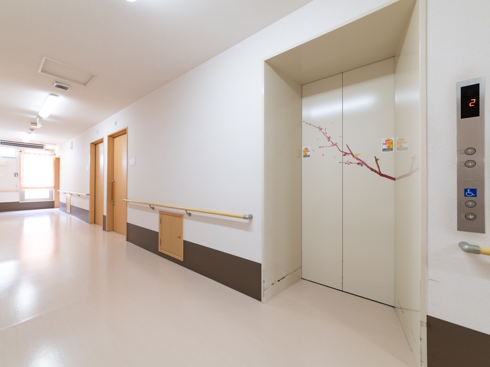 広い通路にエレベーターが設置されている。扉には花の咲いた枝などが描かれている。脇には昇降ボタンが設置されている。