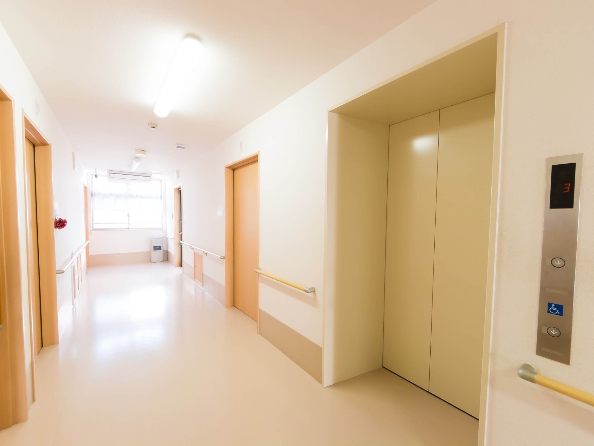 照明が明るく、窓から光が差し込む廊下になっている。入口が広いエレベーターが設置されていて、壁には手すりも付けられている。
