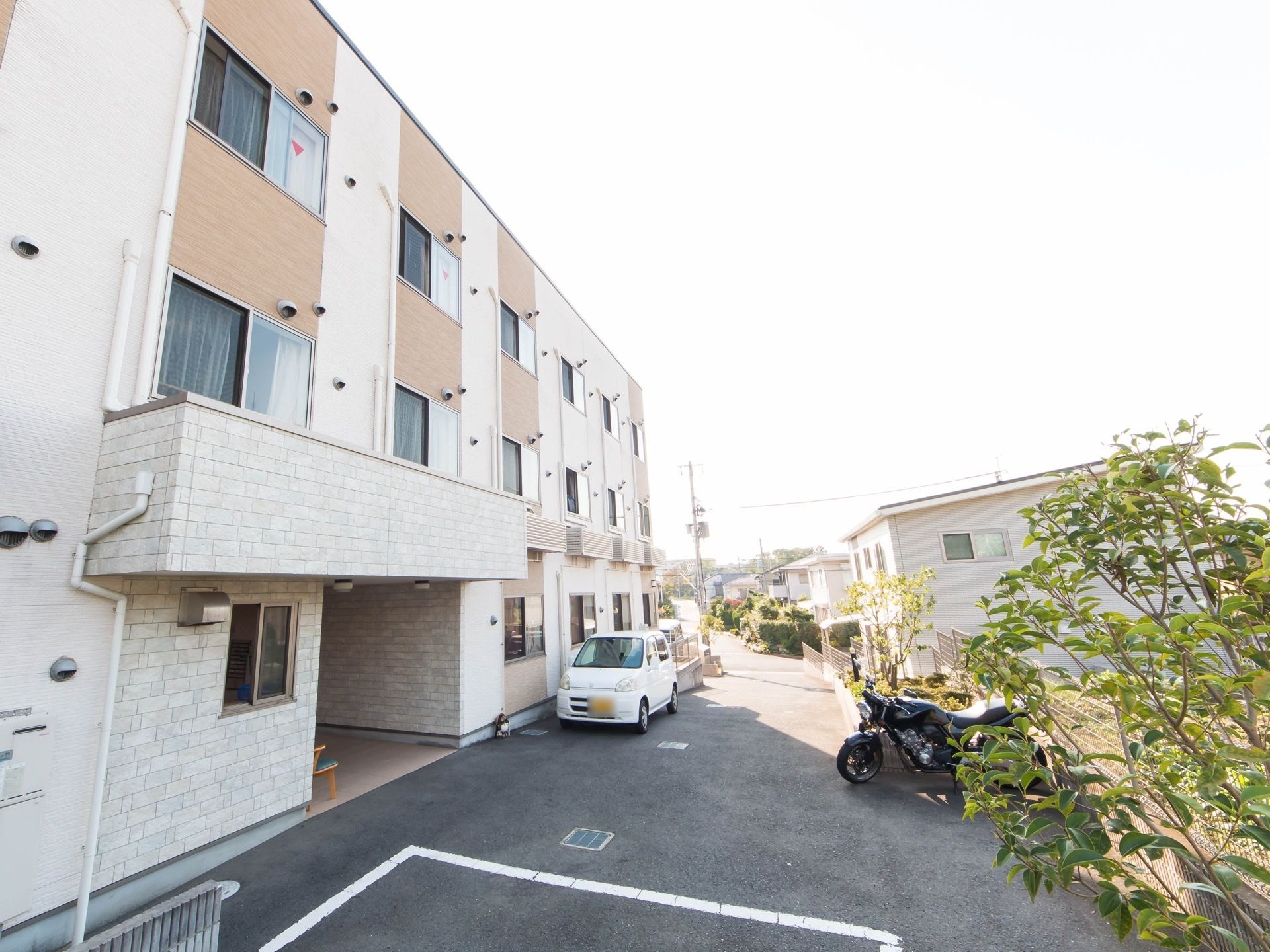 バイクと自動車が施設の前に置かれている。駐車場が広く、玄関の近くまで車が停車できるように構築されているので安心感がある。