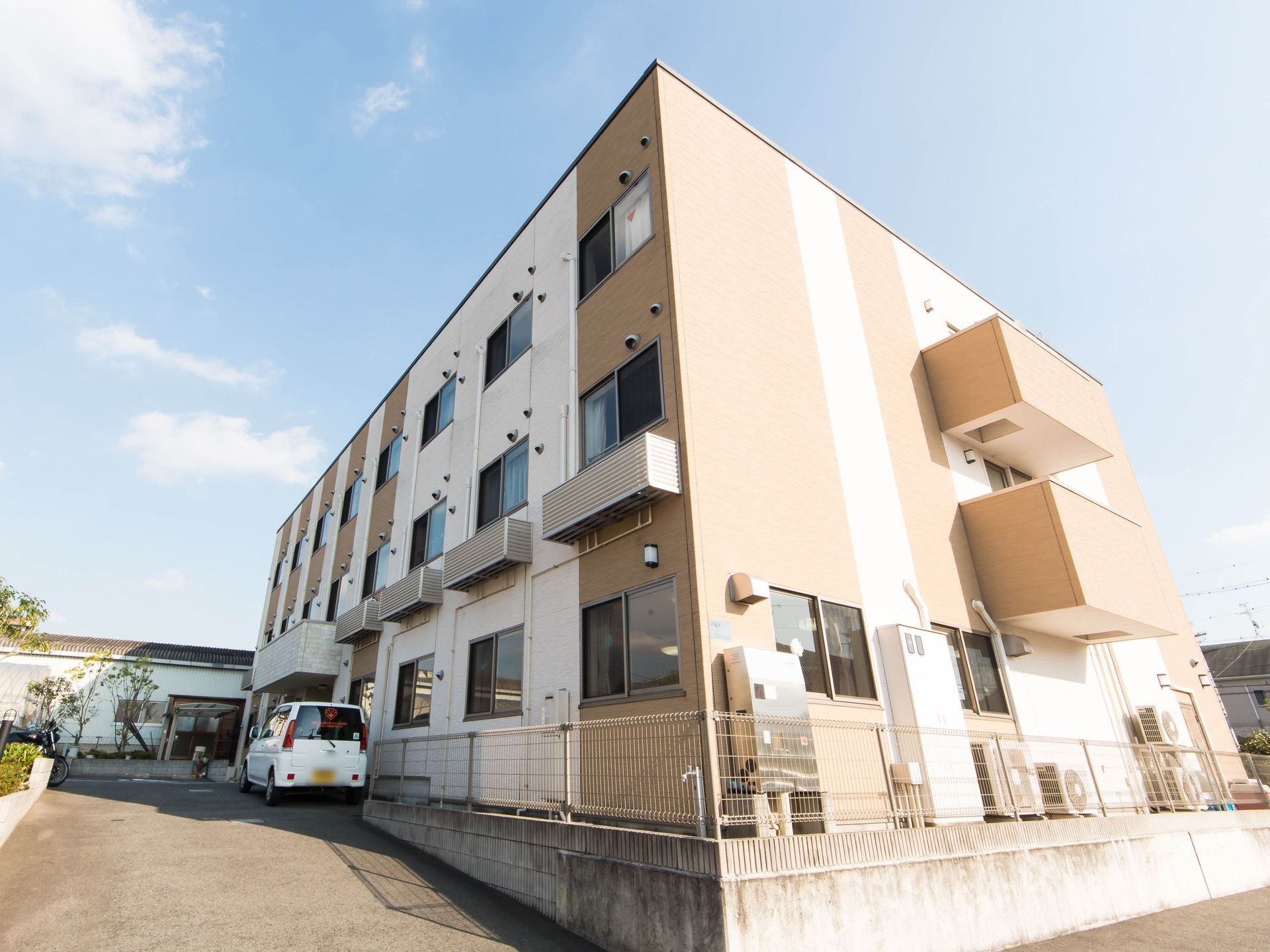 施設の周囲が柵で覆われている。入口には植物が綺麗に植えられており、車の出し入れも便利な広さになっている。