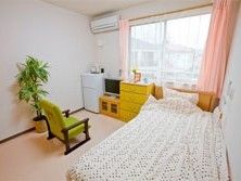 個室内にベッドと椅子、冷蔵庫やテレビなど生活用品がそろっている様子