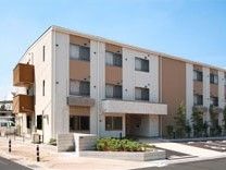 縦にツートンカラーを施したやわらかい色合いの建物。サービス付き住宅ひまわりの外観写真