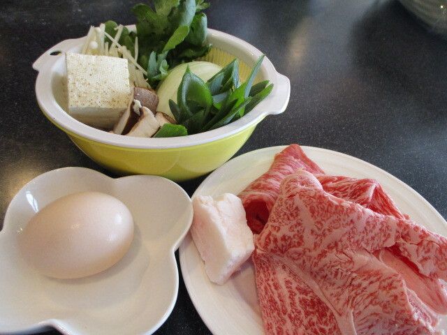 牛脂とスライスした牛肉、たまごと豆腐や野菜など、すきやきの具材が盛られた皿
