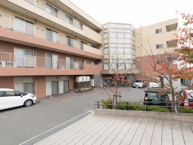 外壁はシンプルな黄色と茶色が落ち着きがある。玄関前は駐車場スペースとなっている。介護付きの老人ホーム。