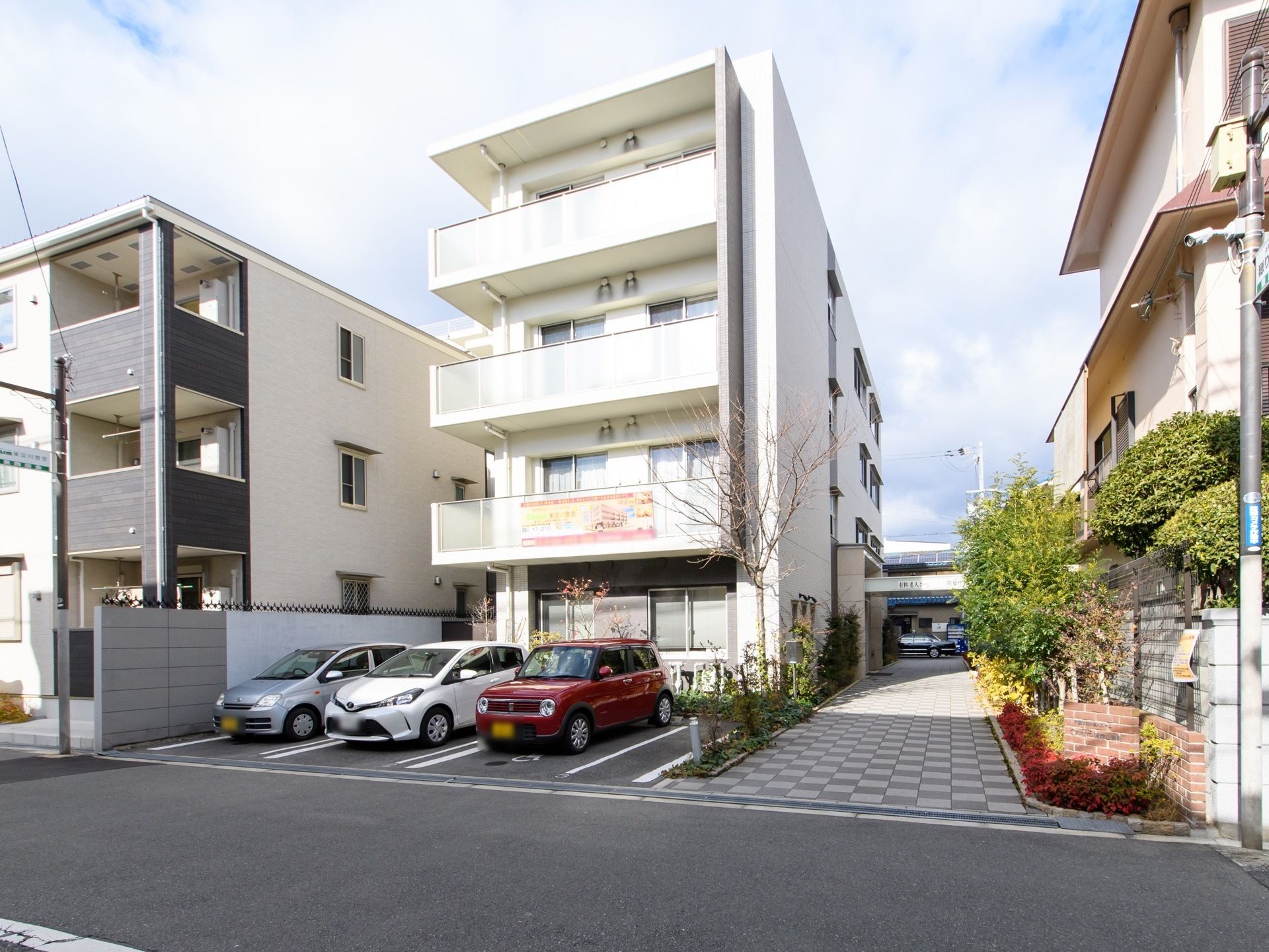白い清潔感のある建物で、バルコニーが設置されている。バルコニー側は遮るものがないので、明るい日差しが当たっている。