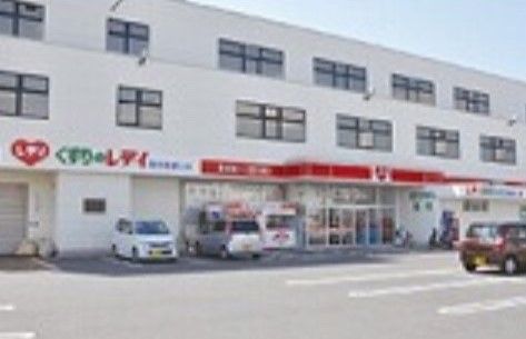 赤い看板が目を引く、出入り口前に広い駐車場を設置した3階立ての薬局の建物