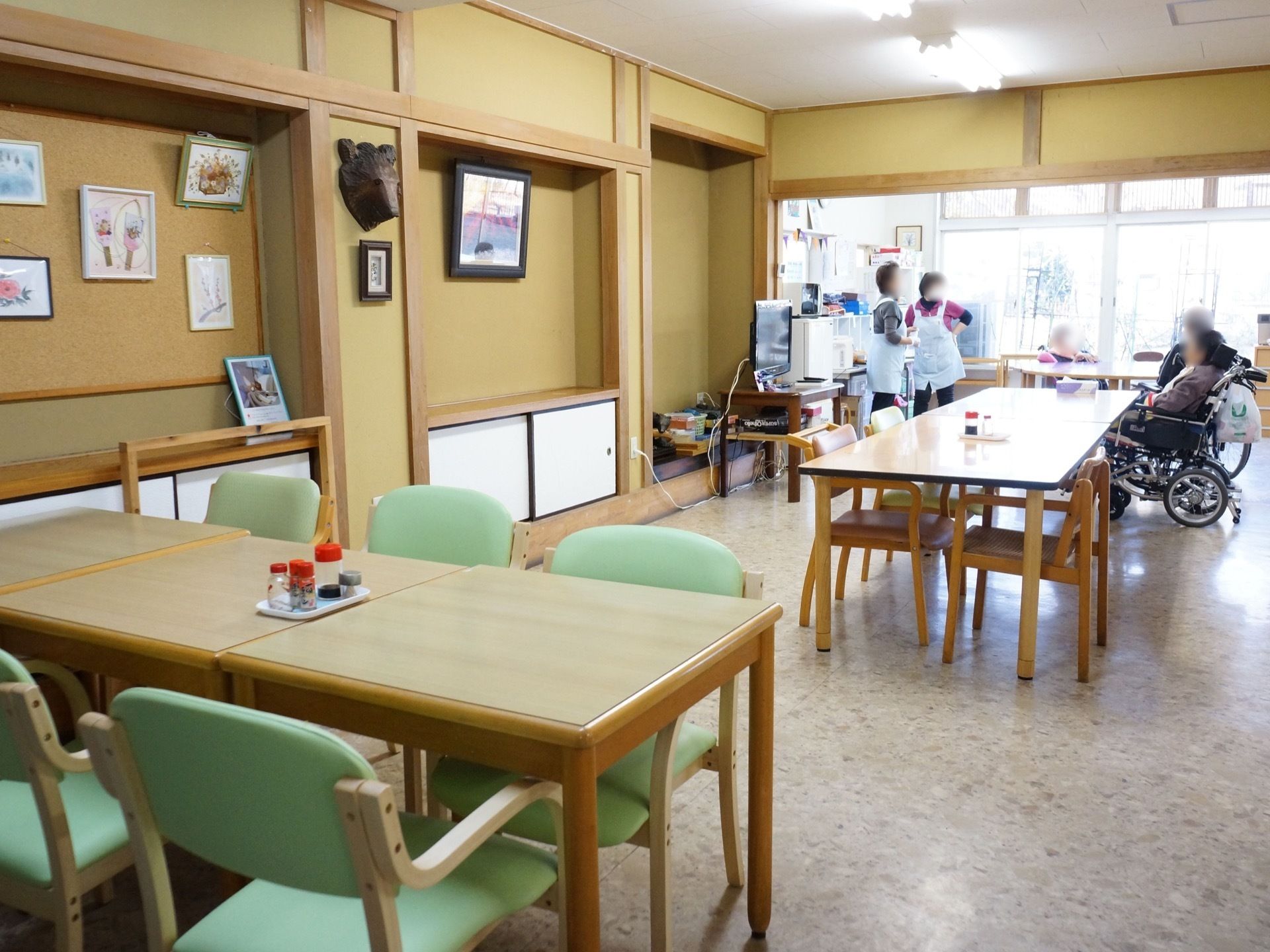 食堂でスタッフを含め数名の入居者様が談笑をしている写真。テレビが設置され、お食事以外の時間も自由に使うことができる。