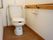 フローリングのトイレには洋式トイレが設置されている。壁にはトイレットペーパーホルダーと手すりが取り付けられている。