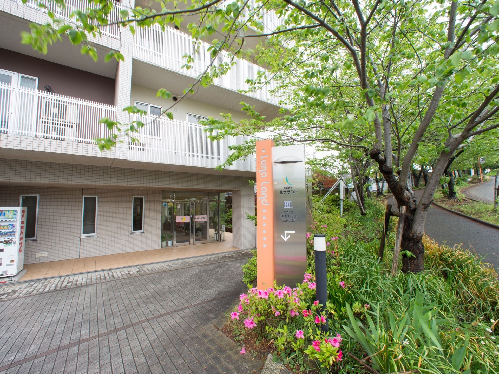 玄関前にある施設名が書かれたステンレスの看板。２階以上の窓の部分には、白い柵が取り付けられたベランダが設置されている。