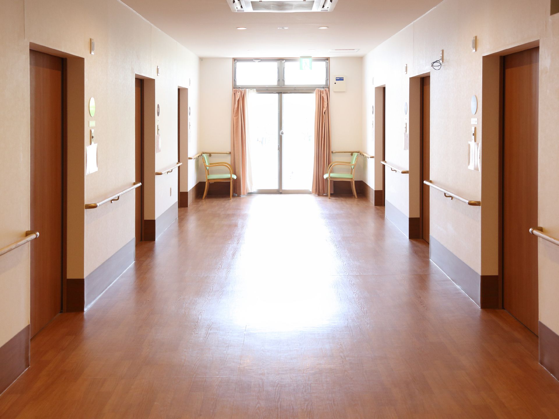 廊下の両側には各3つの部屋の扉が並んでいる。壁側には手すりが取り付けられている。廊下の角には椅子が置かれている。