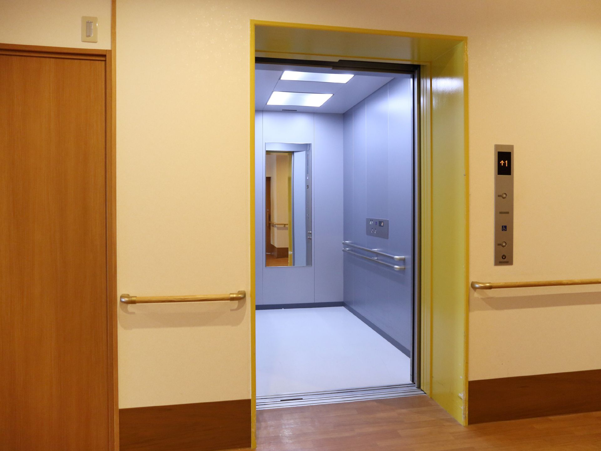 黄色いふちのエレベーターがある。内部は薄い紫色になっている。鏡や2段の手すりが壁に取り付けられている。
