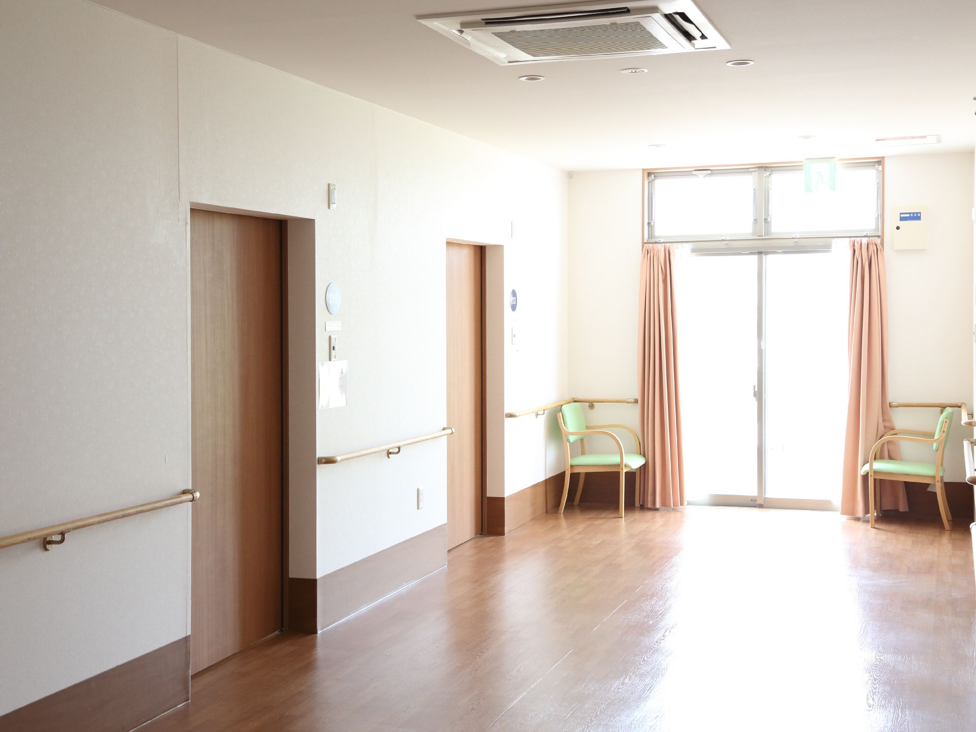 大きな窓がある。窓にはピンクのカーテンがかかっている。カーテンのすぐ横には肘置き付きの椅子が2脚置かれている。