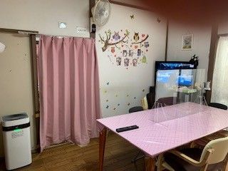 中央に木製のテーブルがあり、周囲に椅子が置かれている。テーブルの上にはカレンダーやティッシュなどが用意されている。