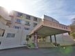 施設名が書かれた屋根が設置されている玄関で、両サイドに花壇がつくられている。目の前の道はアスファルトで舗装されている。