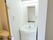 トイレの入口に手すりが設置されている。隣には洗面台がある。全体的に白で統一されているので蛍光灯が映え明るい。