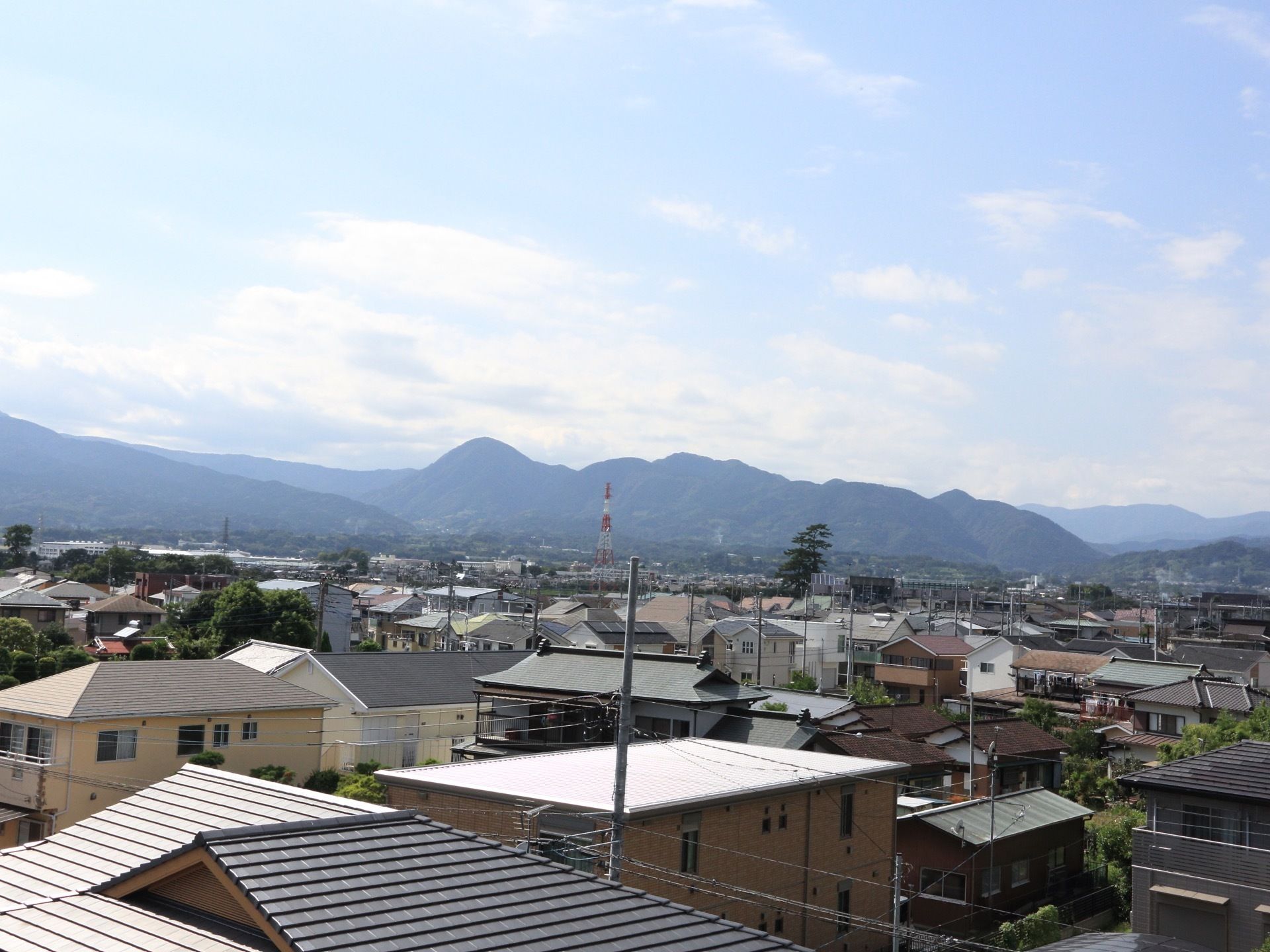 近辺には、高い建物がなく目下に住宅街が広がっている。遠方中央には、鉄塔が建っており奥には山々が連なっている。