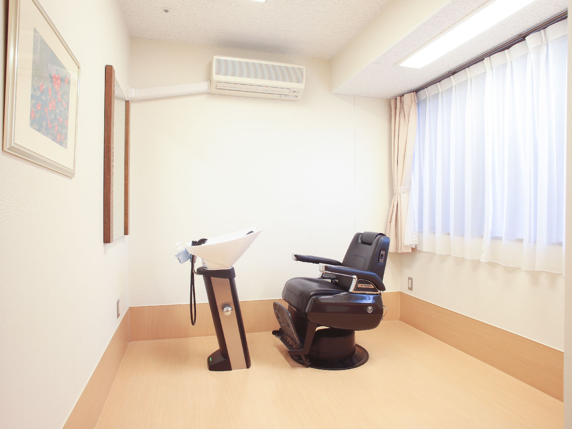 白色の天井と壁に木目の床の内装に黒色の理美容室用の椅子が置かれている。横一面は窓になっていて、壁には絵が飾られている。