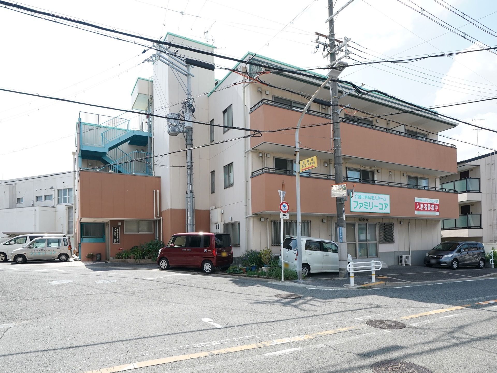 車が数台駐車しており、大通りに面した角地に建つ3階建ての建物