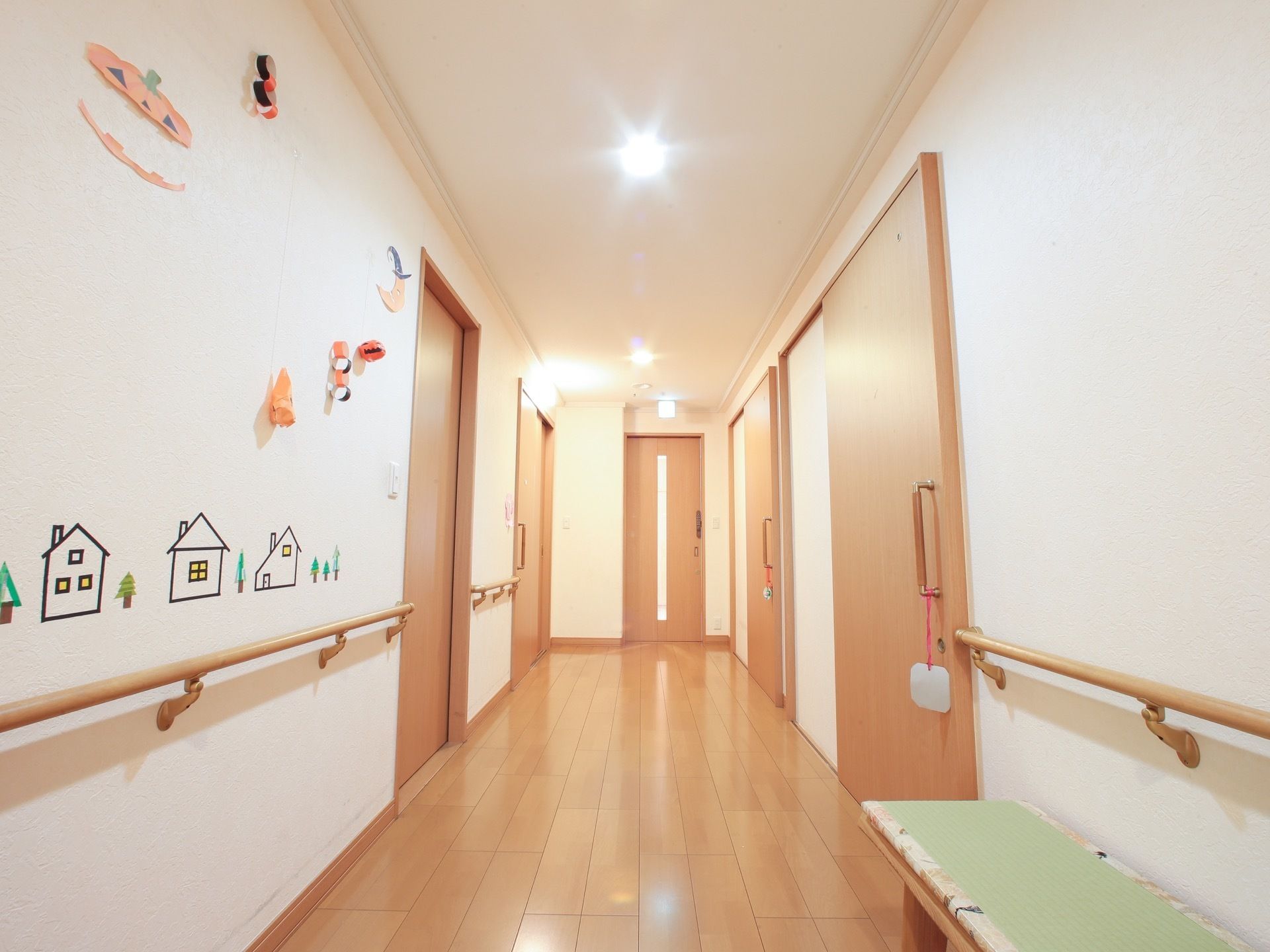 明るく通しの良い廊下の両サイドには、居室のドアが並んでいる。壁には手すりが取り付けられており、ベンチが置かれている。
