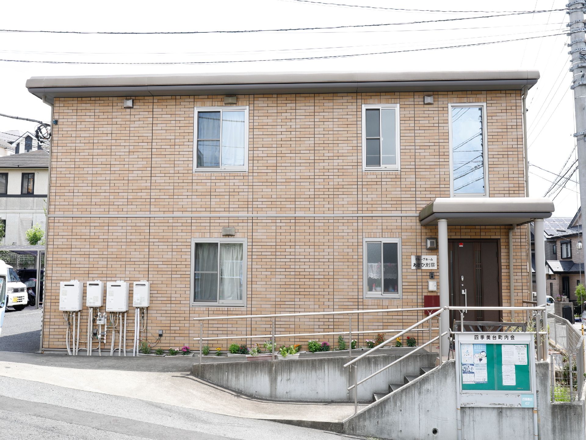 薄い茶系のタイル調の外観の2階建ての建物で、建物の端の所に玄関出入口がある。傍にはアプローチが設置してある。