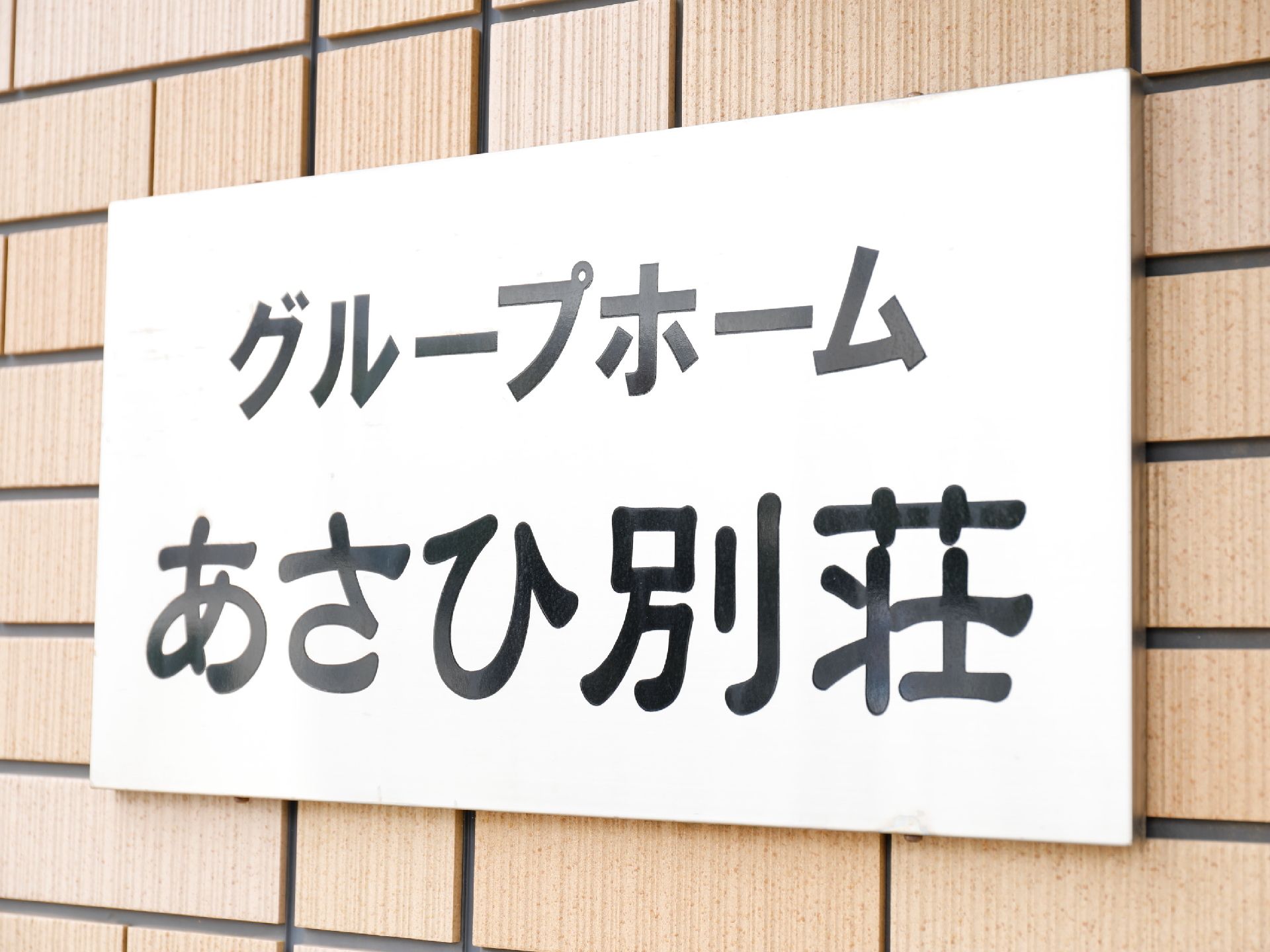 玄関出入口の横に掲げられた施設名の表札で、白地に黒色の文字で表示されている。シンプルで分かりやすくなっている。