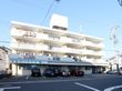 施設の外観はホワイト色で各部屋にはベランダがつけられている。建物の前には駐車場のスペースが設けられている。
